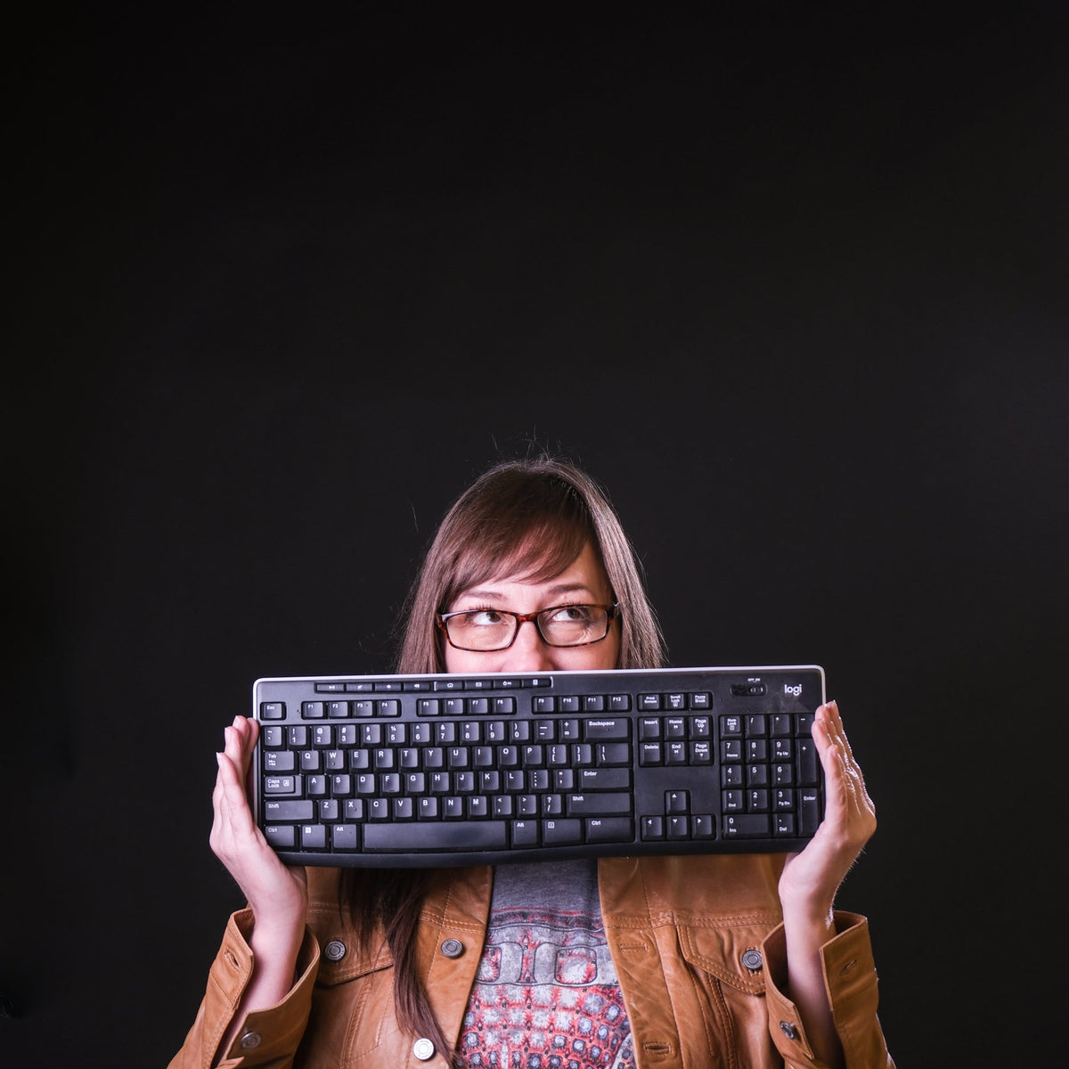 Person holding a keyboard in front of their face on a black background
