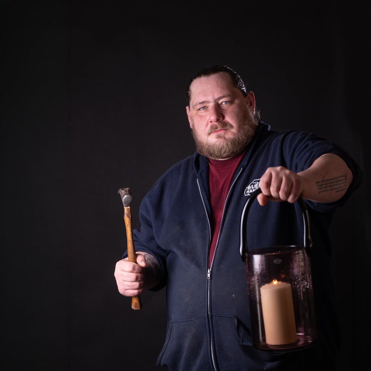 Man holding a lantern and a wooden tool against a black background