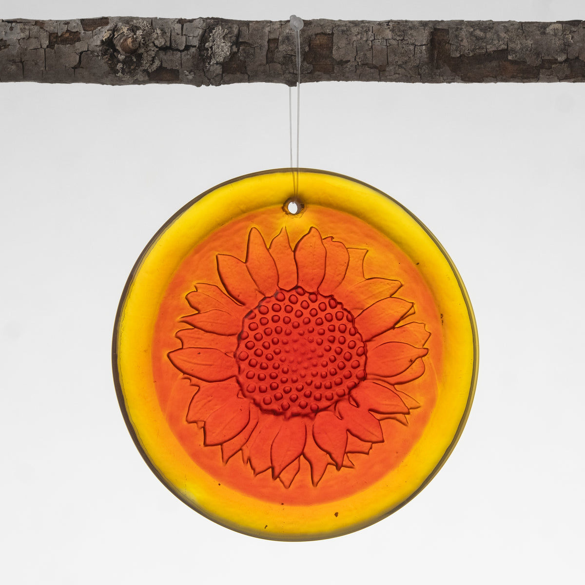 A handmade circular suncatcher with a sunflower design in shades of orange and yellow, hanging by a string.