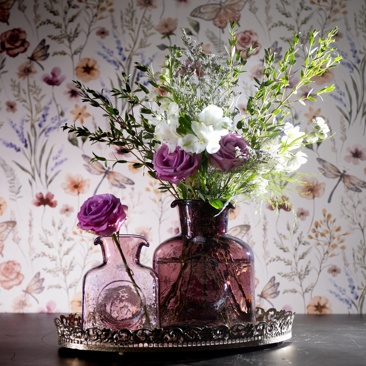 Decorative purple vase with flowers on a table against a floral wallpaper background