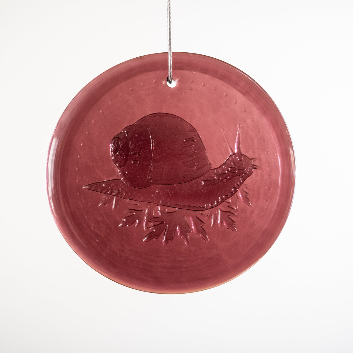 Round red glass ornament with a snail design on a white background
