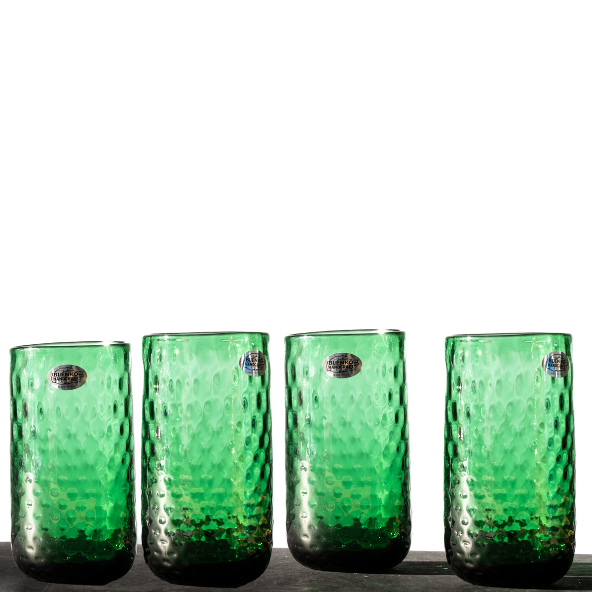 A set of four green hand-blown glass tumblers with a diamond optic pattern, displayed side by side.