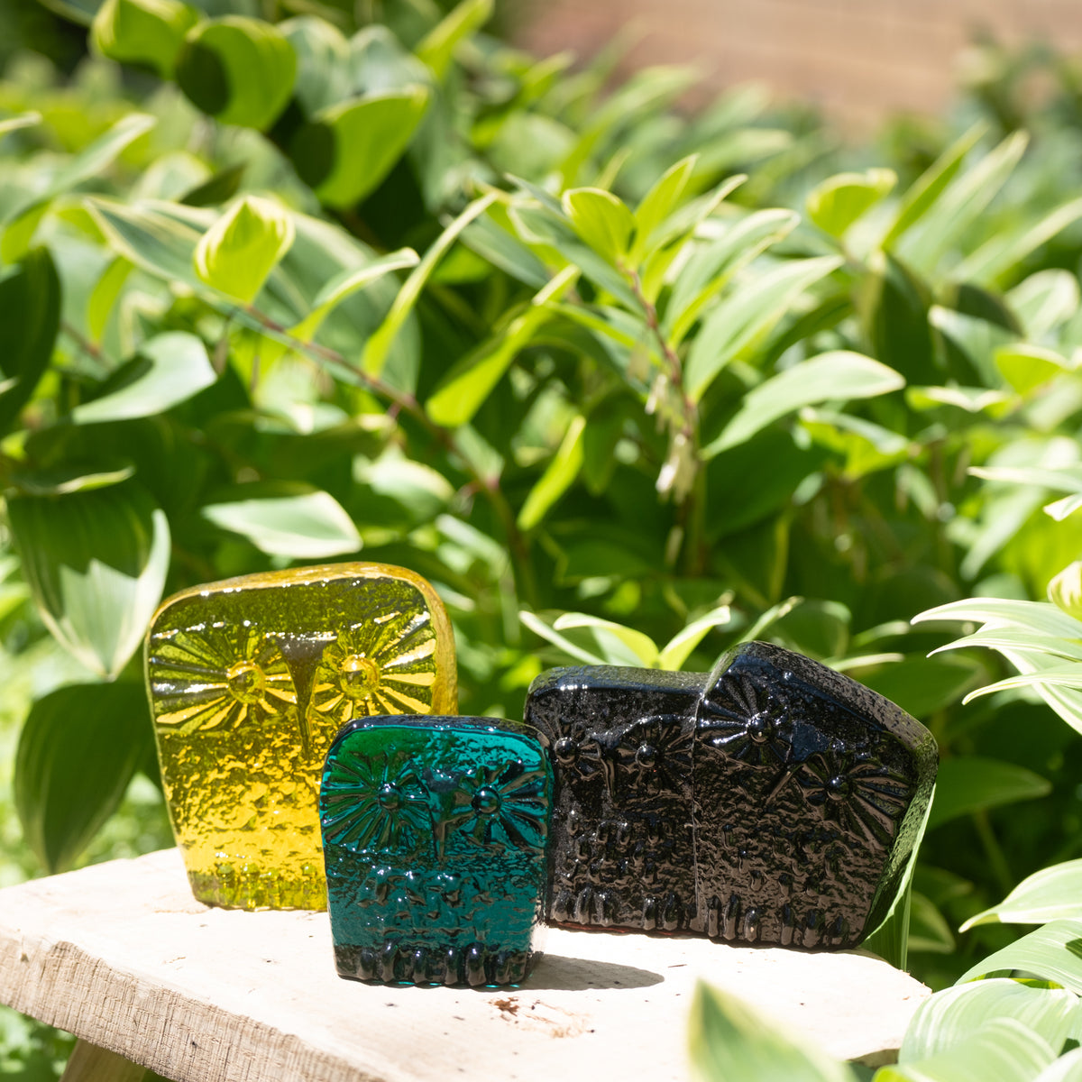 Three colorful soap bars on a wooden surface with green foliage in the background