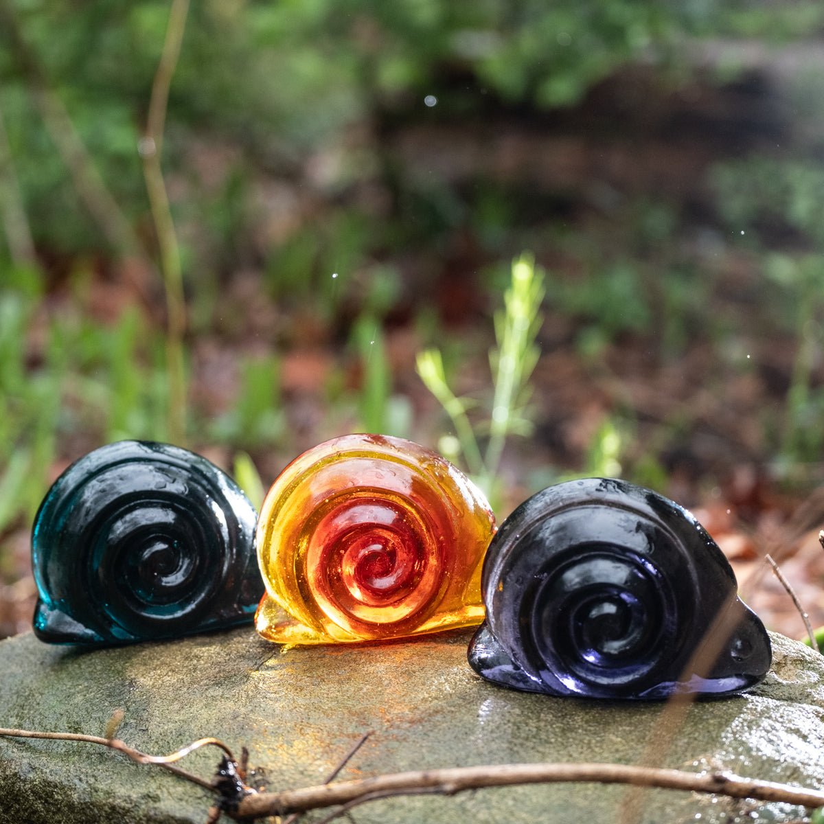 handcrafted glass snail figurines on a rock outside