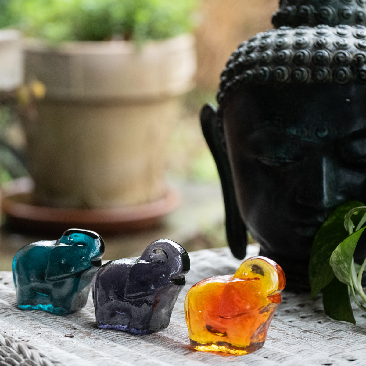 Three colorful elephant critters on an outside table with a face sculpture in the background.