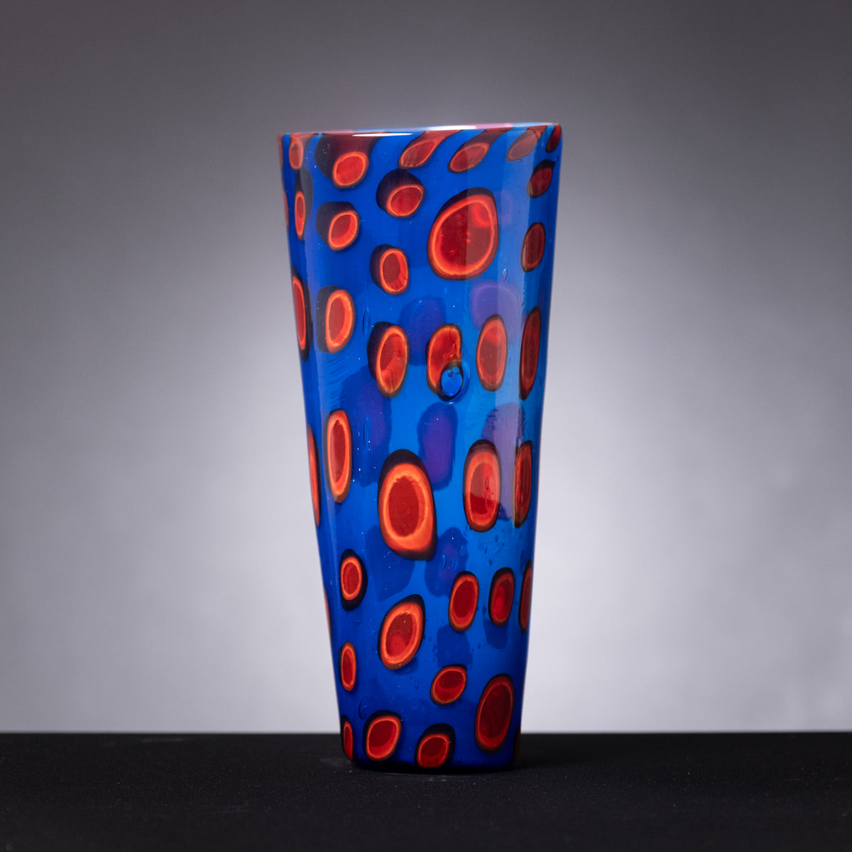 Blue glass vase with red circular patterns on a gray background