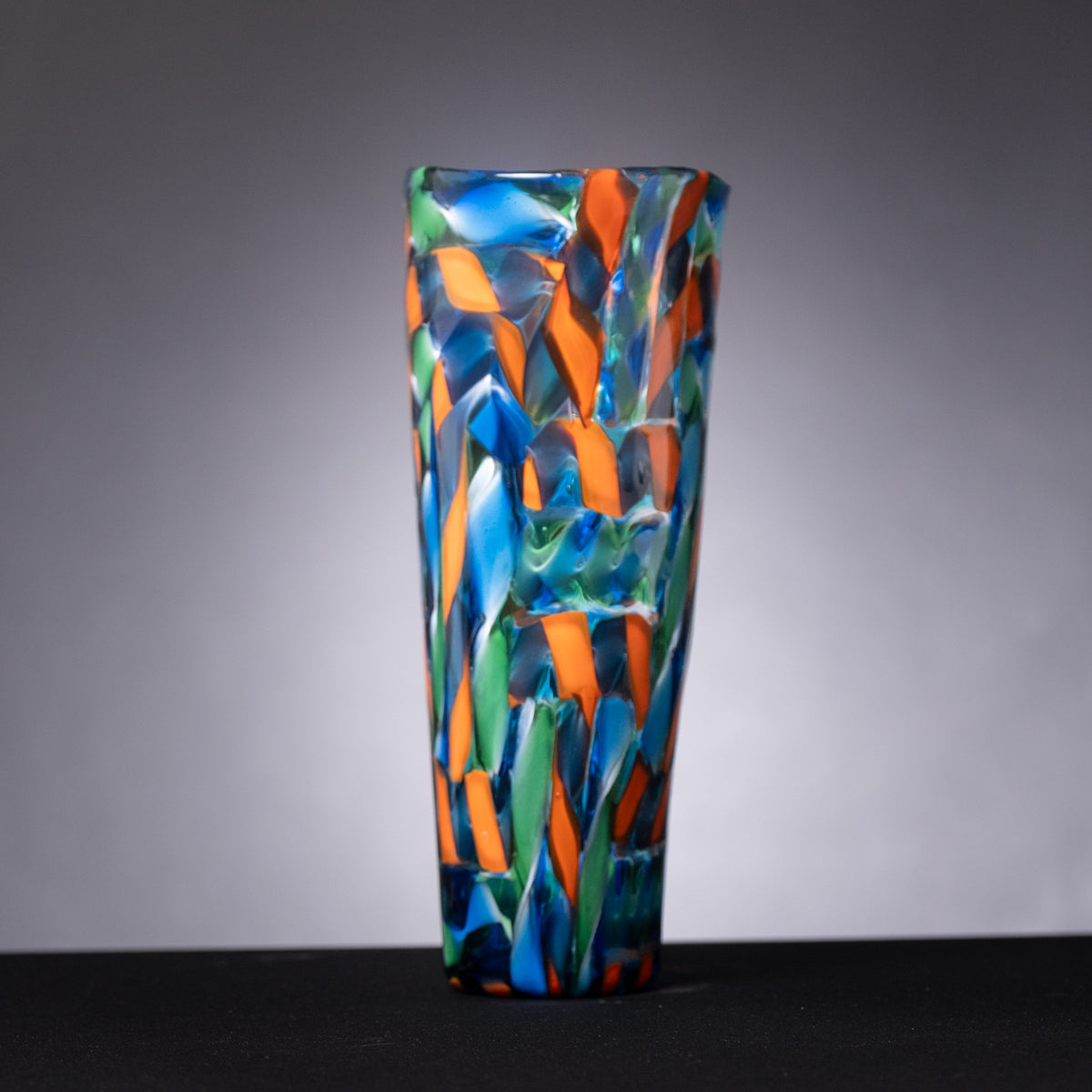 Colorful glass vase with blue, orange, and green patterns on a gray background