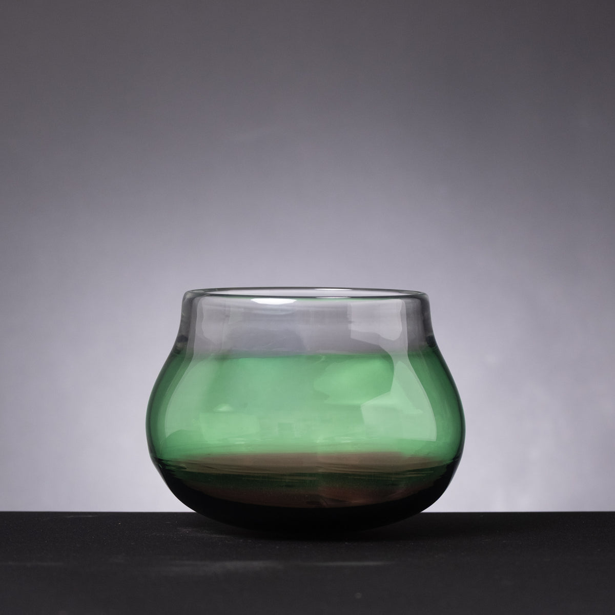Green glass bowl on a dark surface with a gray background