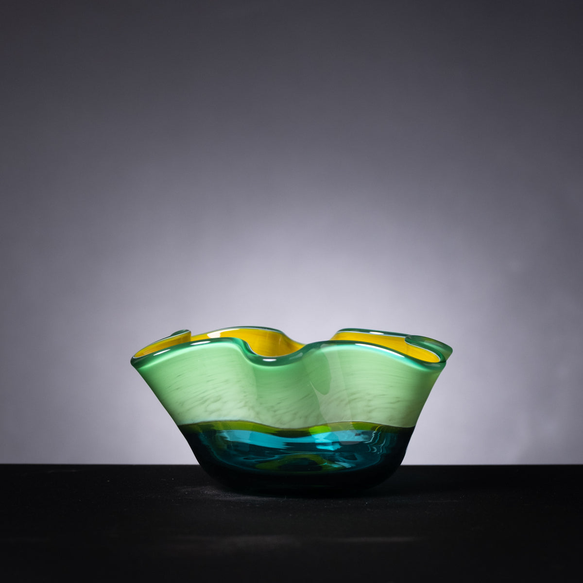 Green and blue glass bowl on a dark surface with a gray background