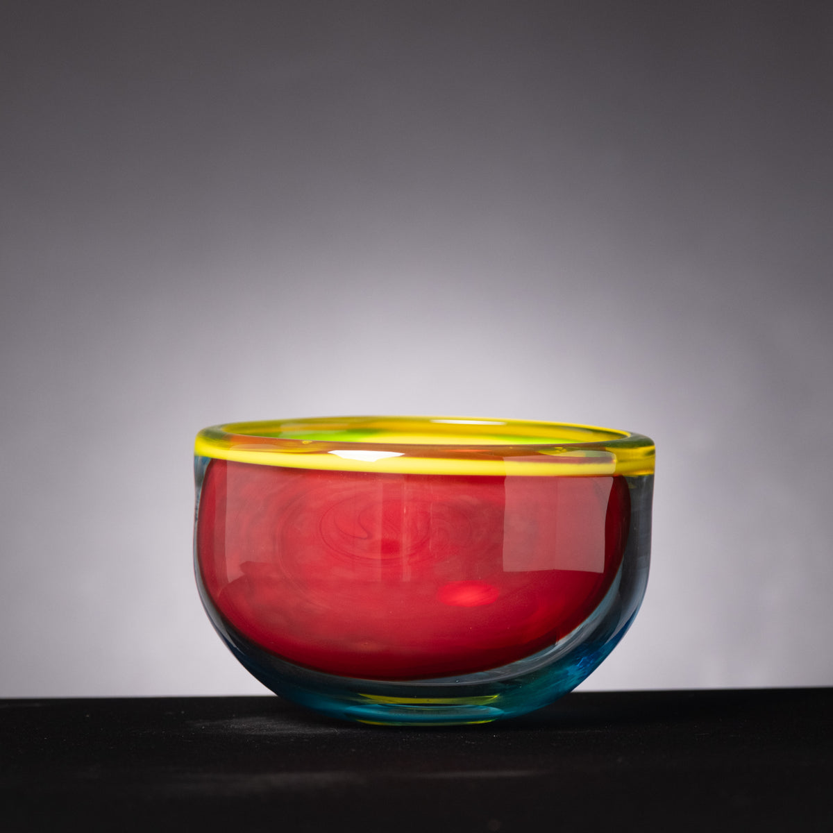 Colorful glass bowl with a gradient from red to blue on a dark surface and gray background