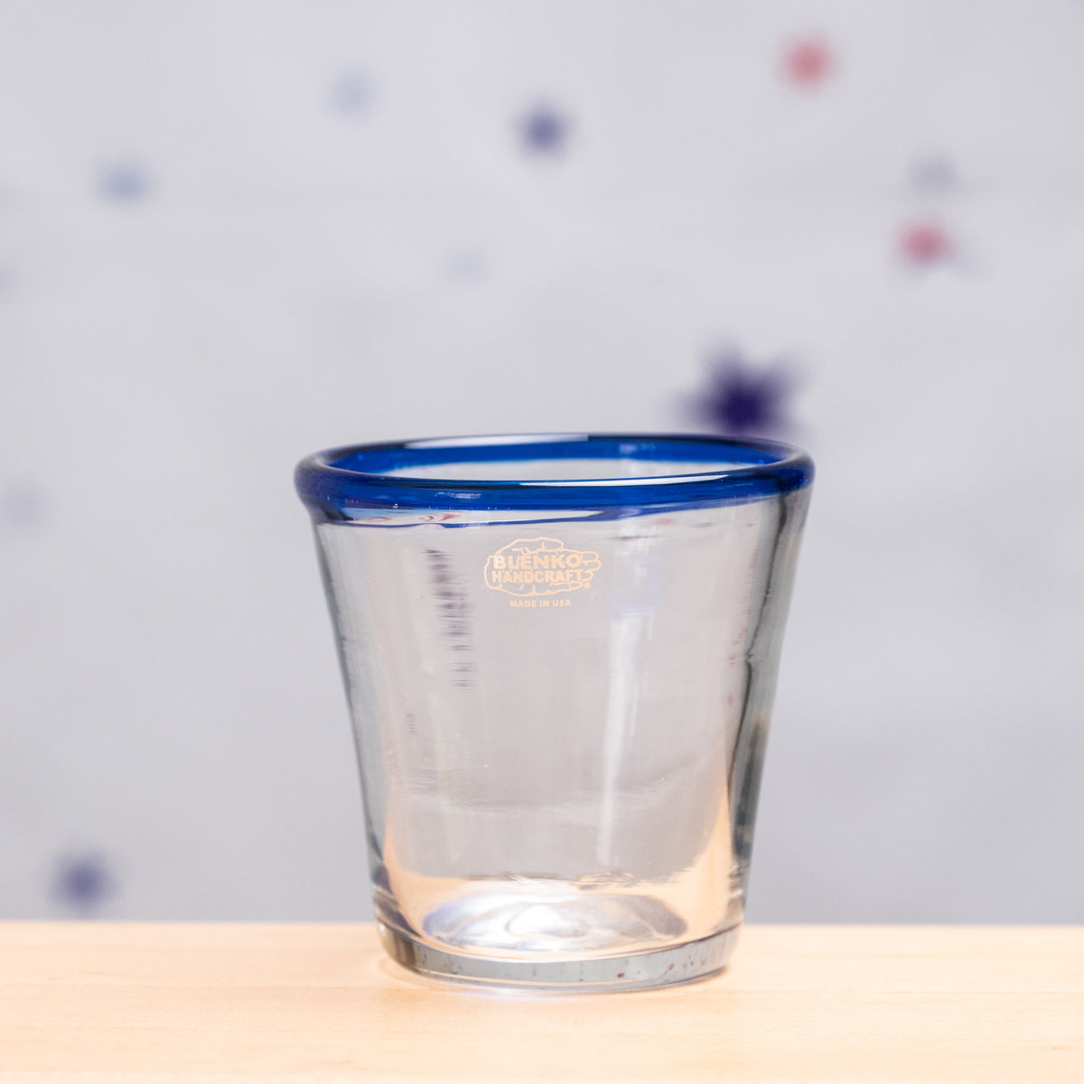 Clear glass with blue rim on a wooden surface and polka dot background