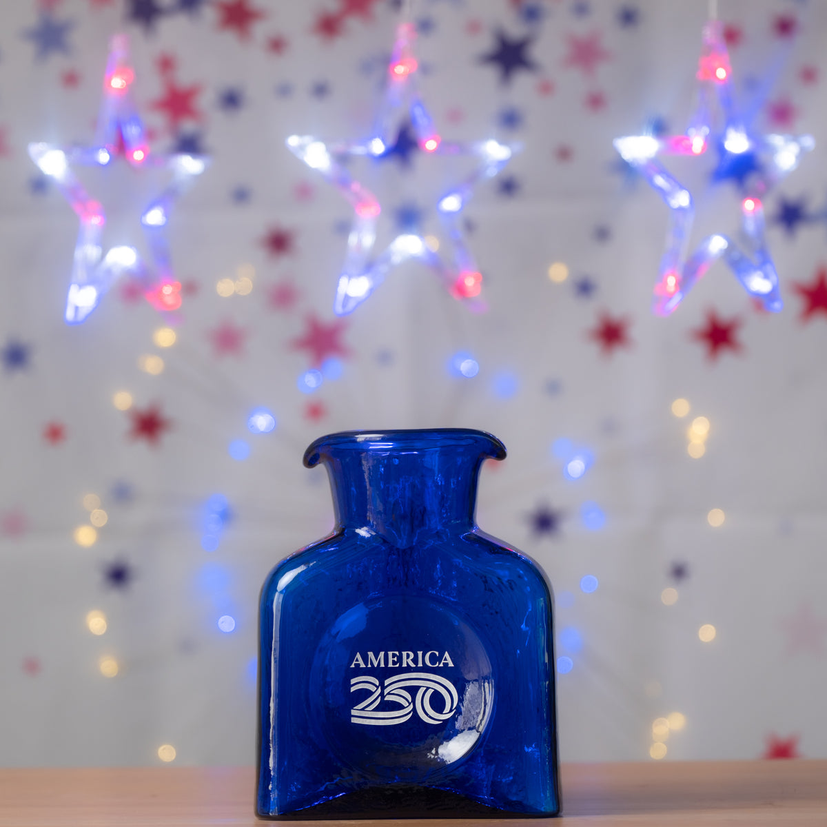 Blue bottle labeled 'America 250' with festive lights in the background