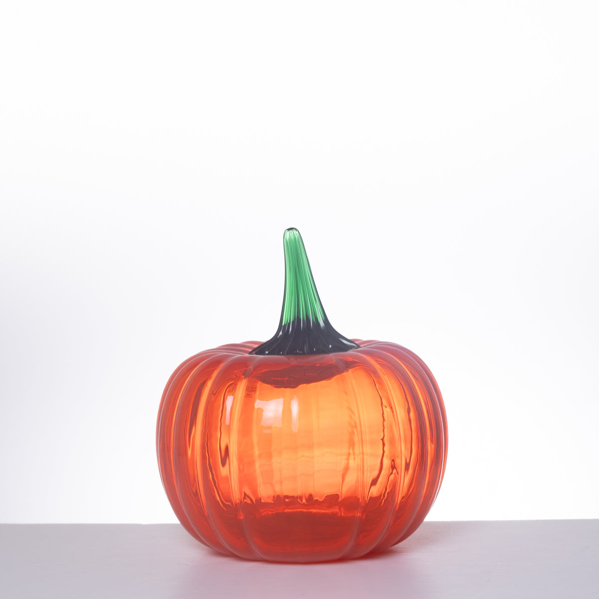 A ribbed glass pumpkin vase with a vibrant orange body and a green stem, set against a plain white background.