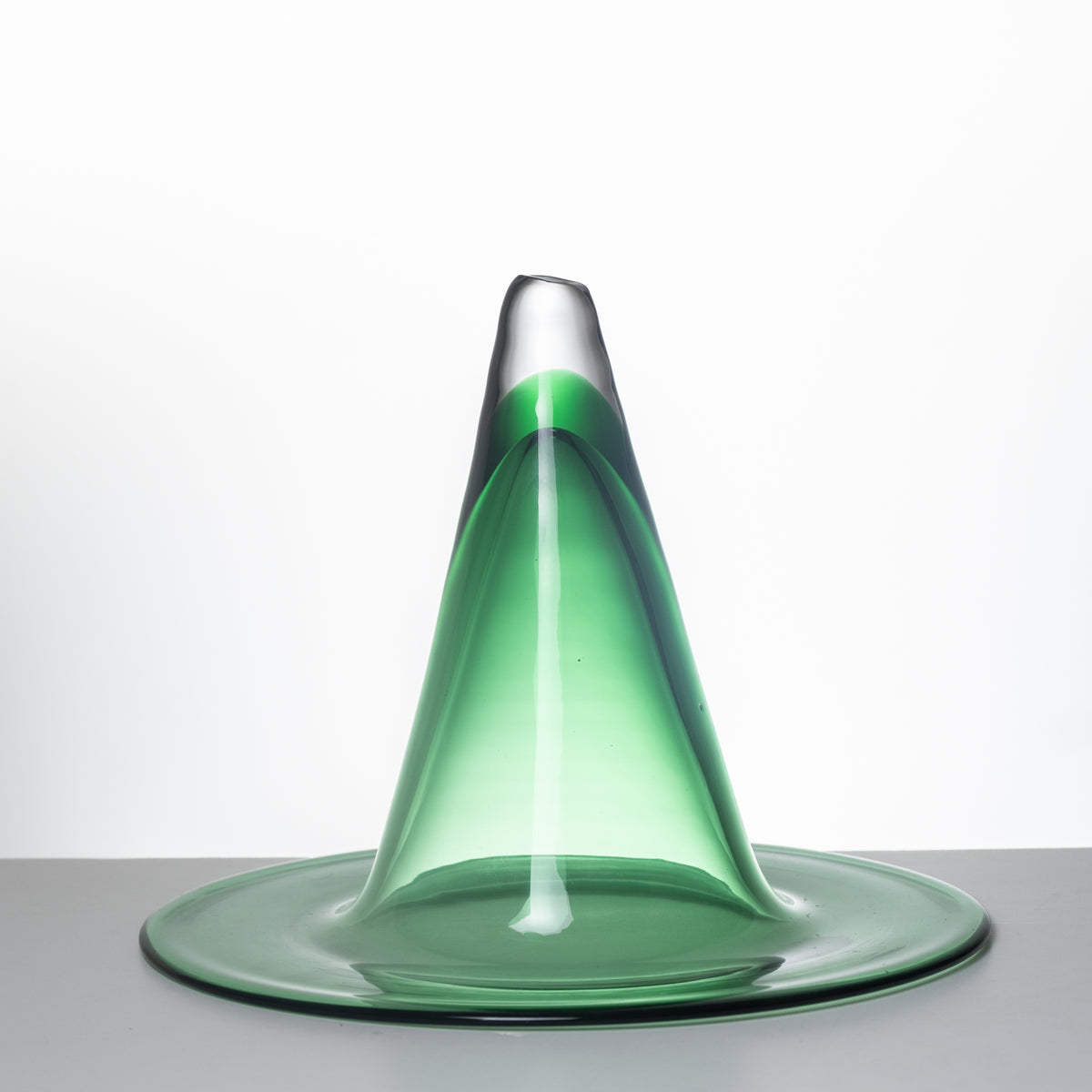 A translucent green glass sculpture shaped like a volcano with a wide circular base, photographed against a clean white studio background.
