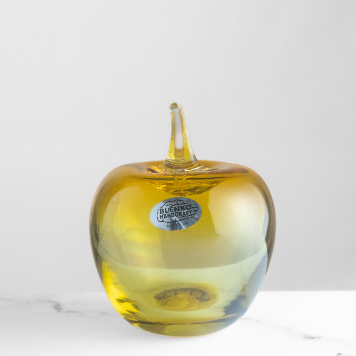 Yellow glass apple with 'Blenko Handcraft' label on a white background