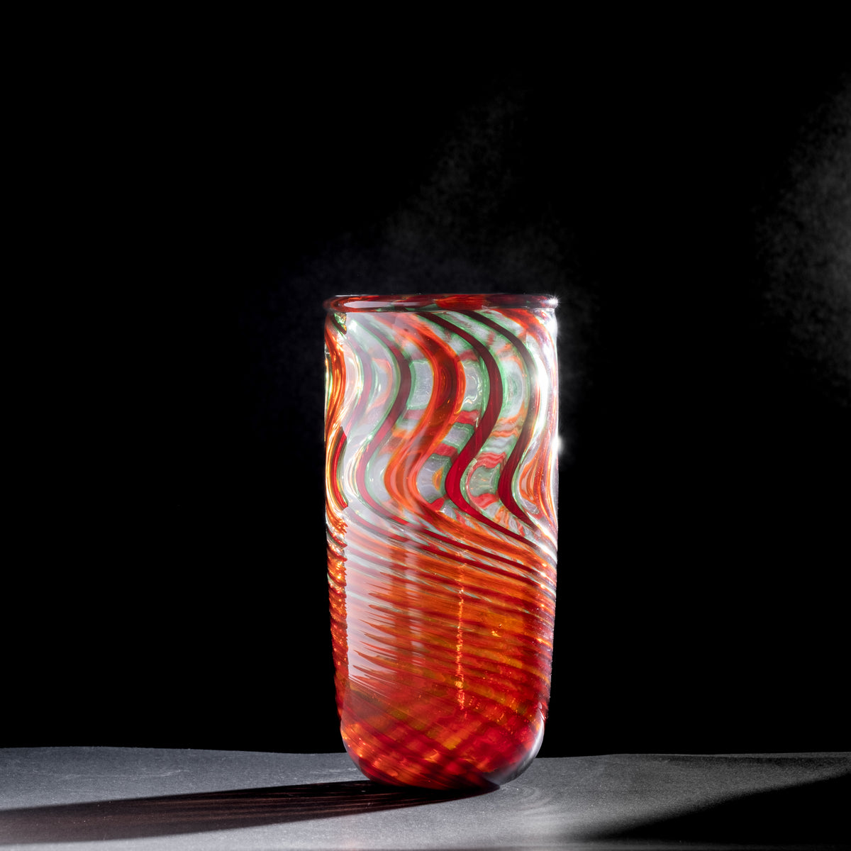 Glass vase with red and green wavy pattern on a black background