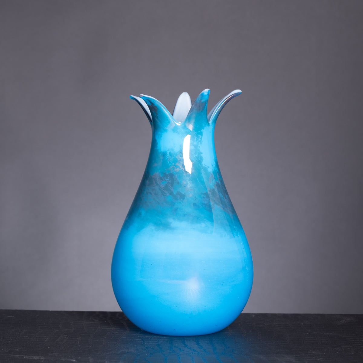 Blue glass vase with a unique design on a dark surface and gray background