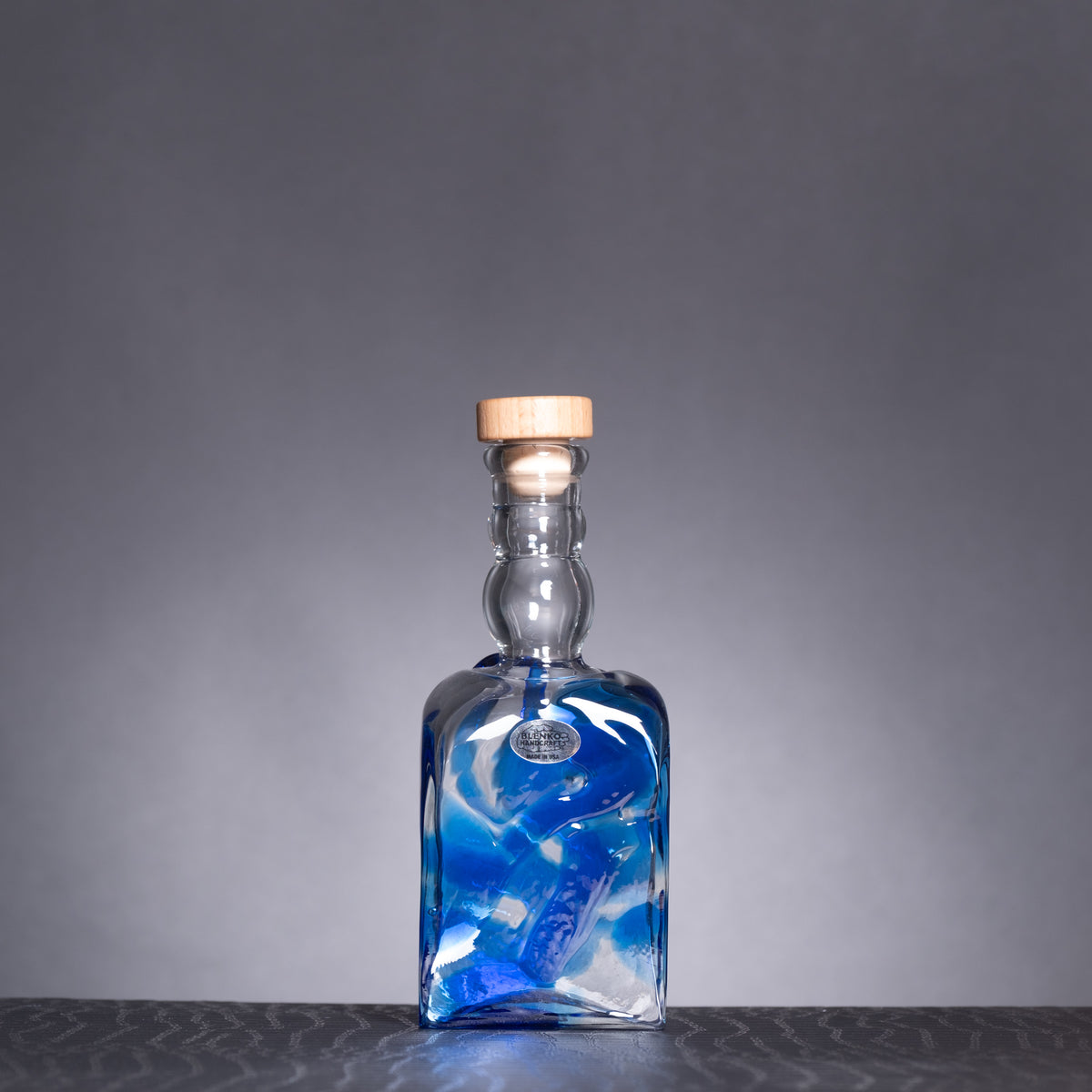 Blue glass bottle with a wooden cap on a gray background