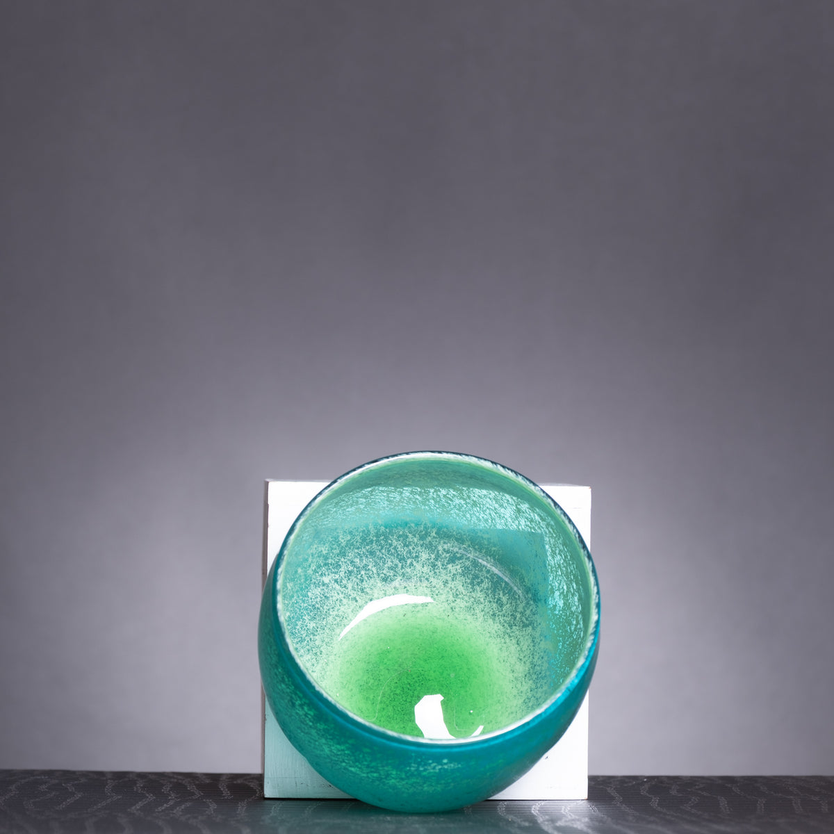Green candle in a textured glass holder on a dark surface with a gray background