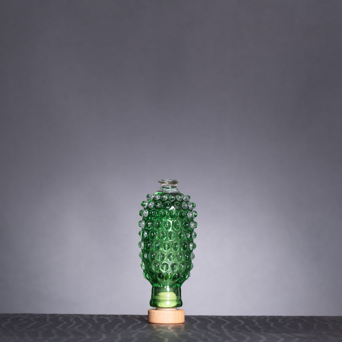 Green textured vase on a dark surface with a gray background