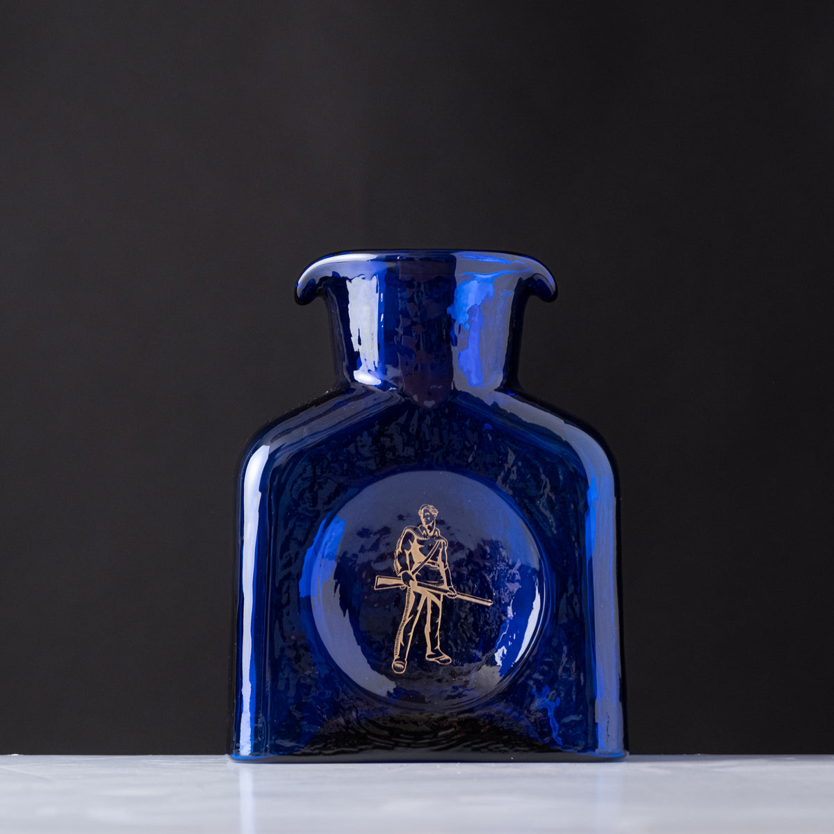 Blue glass bottle with gold emblem on a dark background