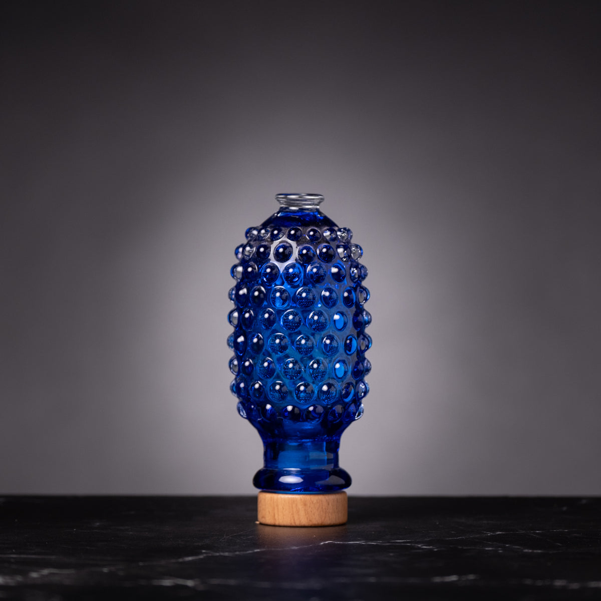 Blue textured glass bottle with wooden base on a dark surface and gray background