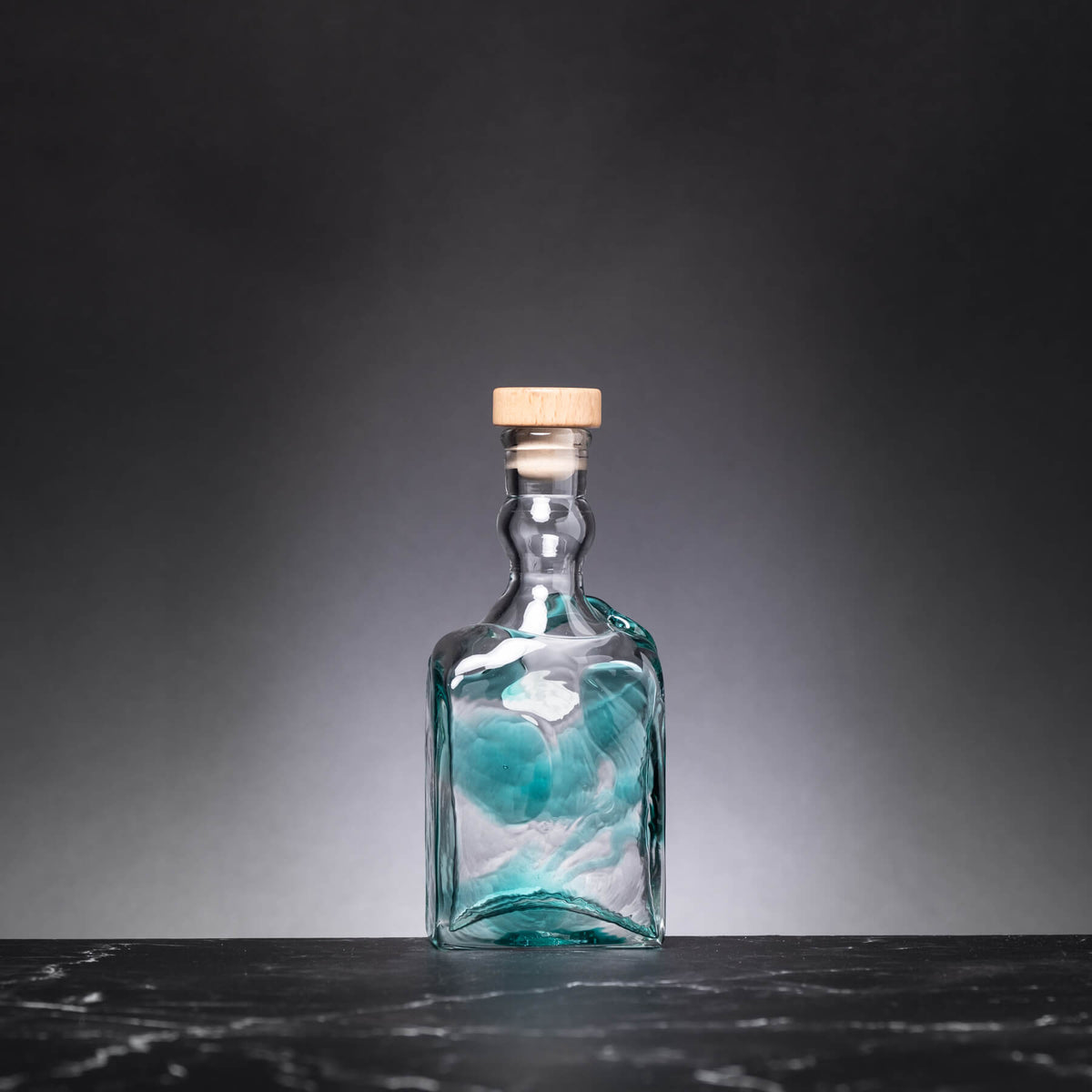 Glass bottle with a cork on a dark surface and gray background