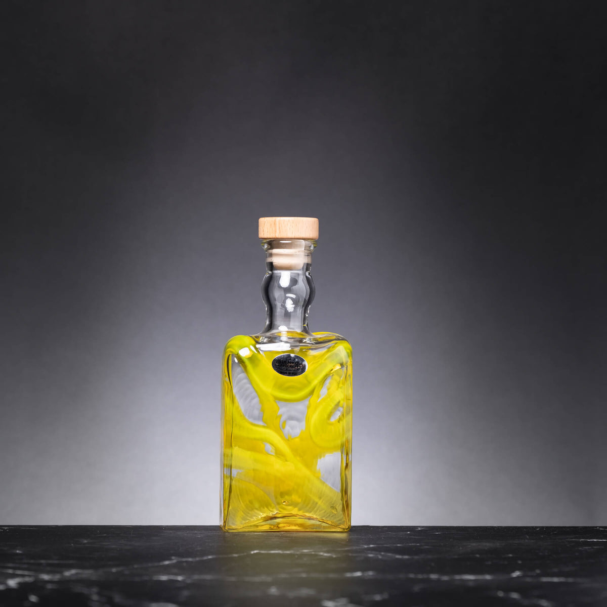 Glass bottle with a yellow design on a dark surface and gray background