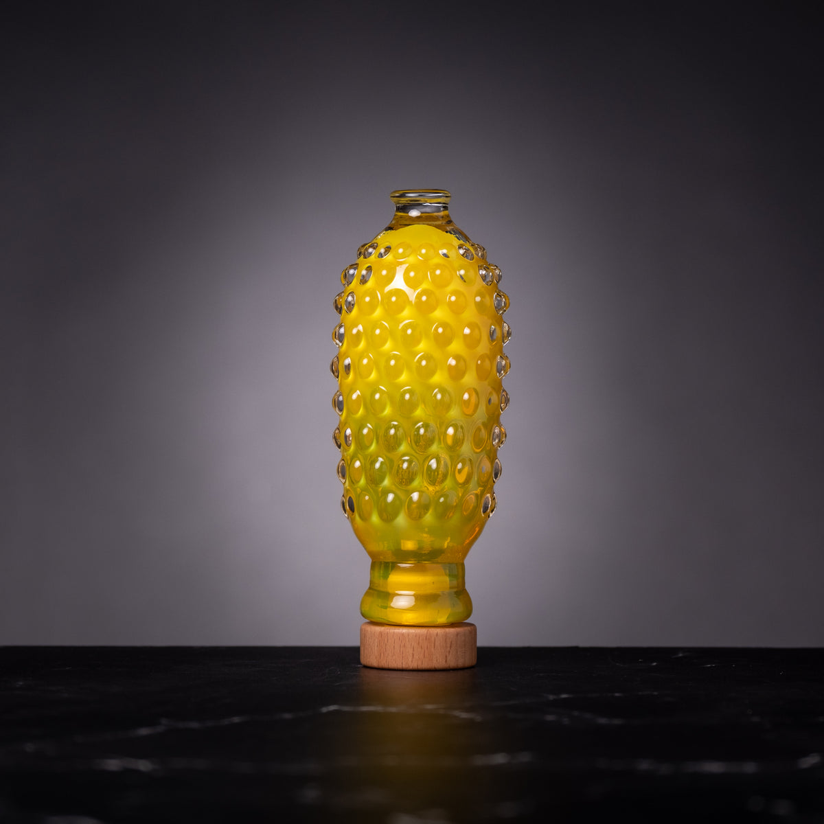 Yellow glass bottle with textured surface on a dark surface and gray background