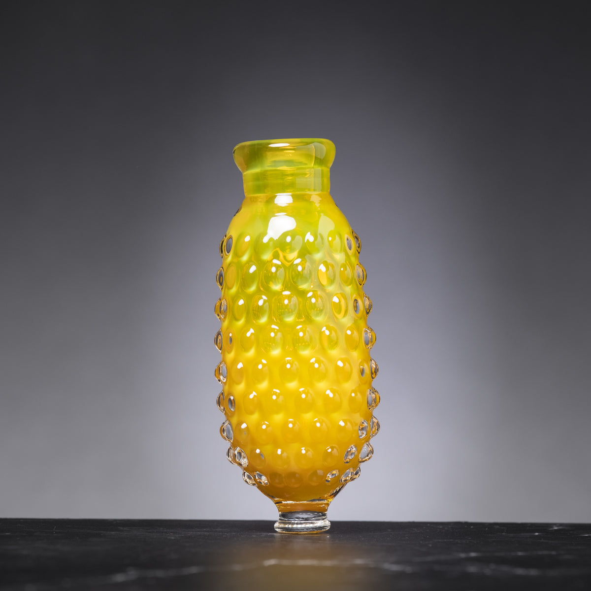 Yellow glass vase with textured surface on a dark surface and gray background