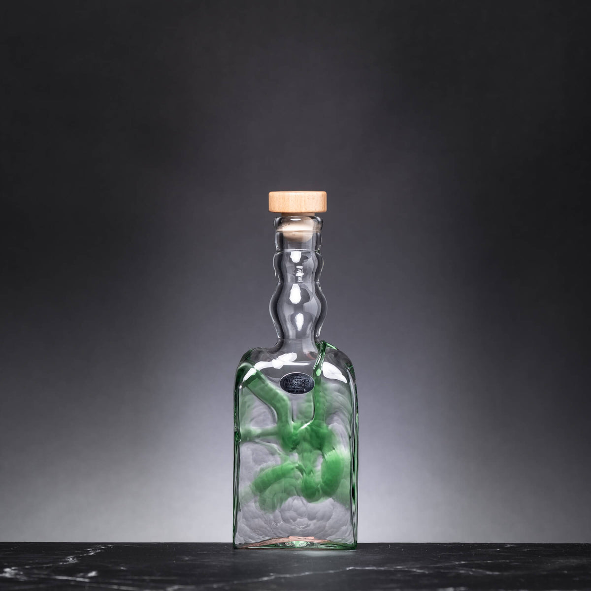 Glass bottle with a cork lid on a dark surface and gray background