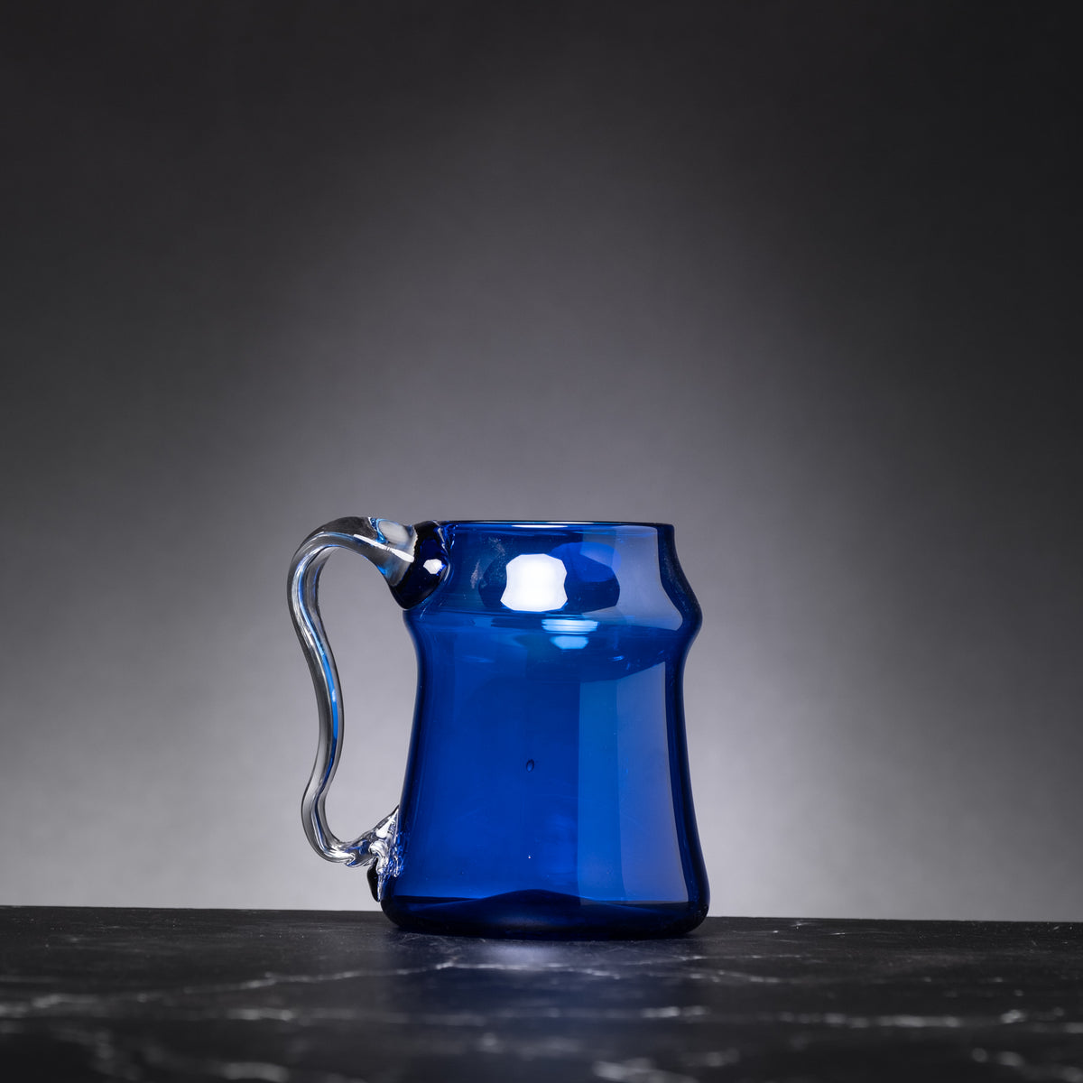 Blue glass mug on a dark surface with a gray background