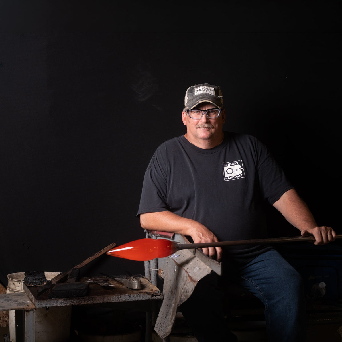 Glassblower in a chair working with glass against a glass background