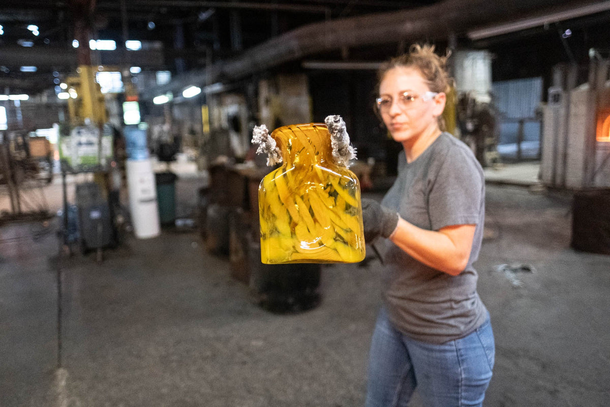 Glassworker carrying a bottle to the lehr to cool off.