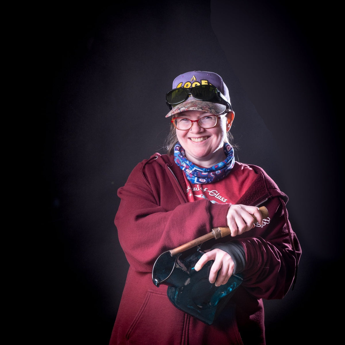Person wearing a red sweatshirt and colorful bandana, holding a pipe against a black background