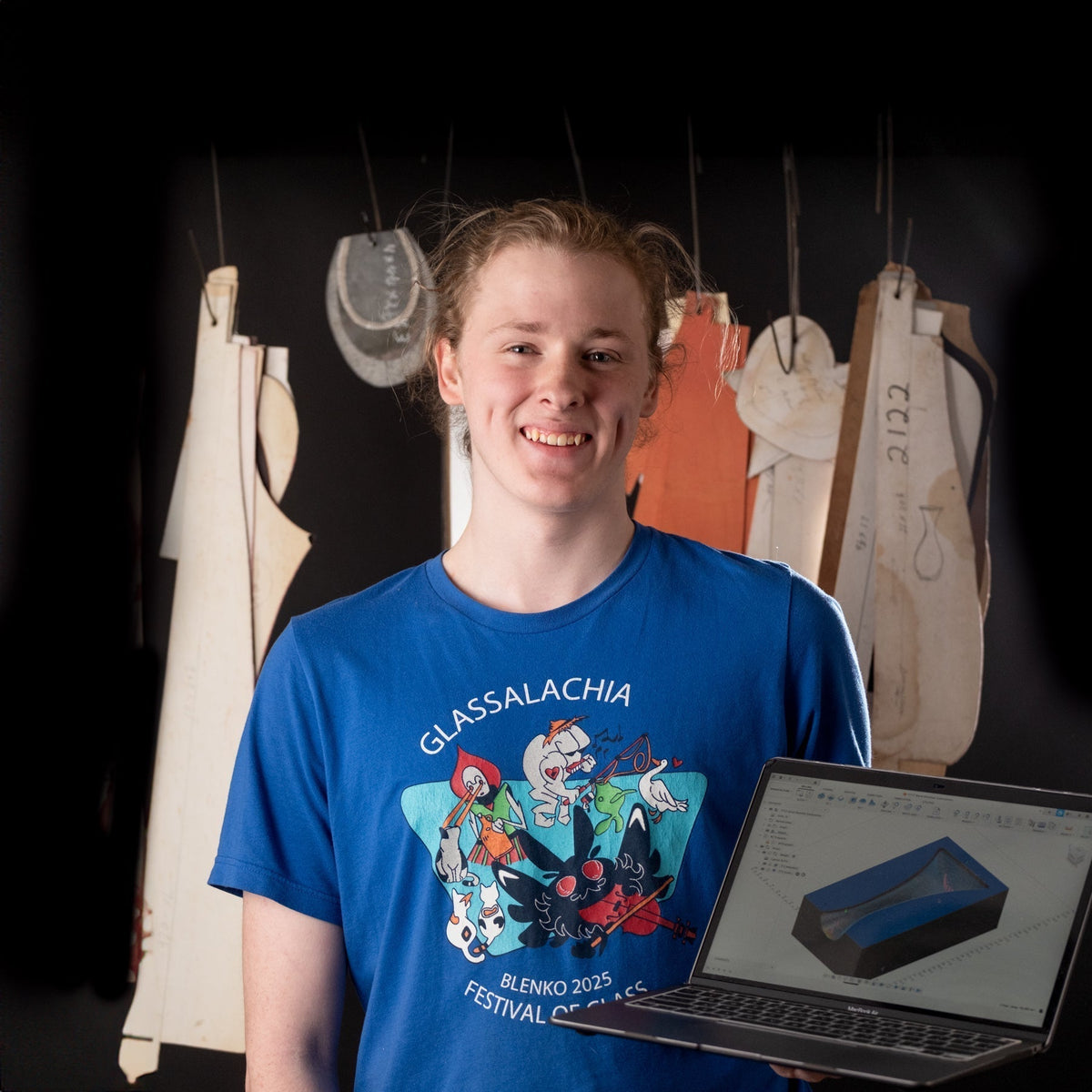 Person holding a laptop with a colorful design in front of a black background with hanging fabrics.