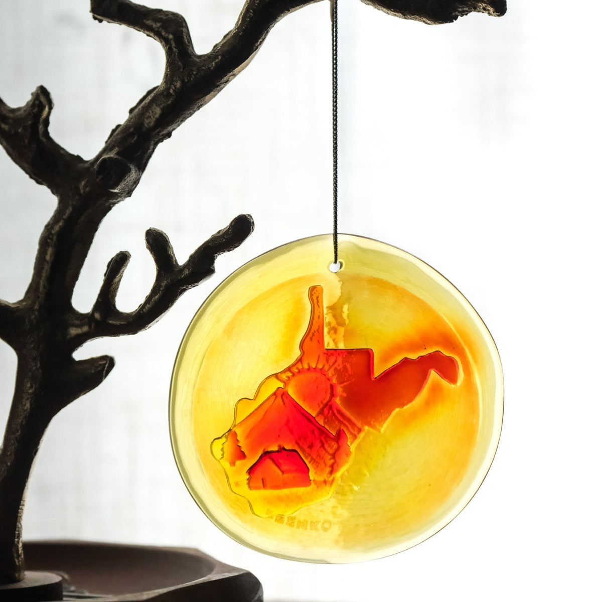 Decorative circular ornament with a red horse silhouette on a yellow background, hanging from a branch.