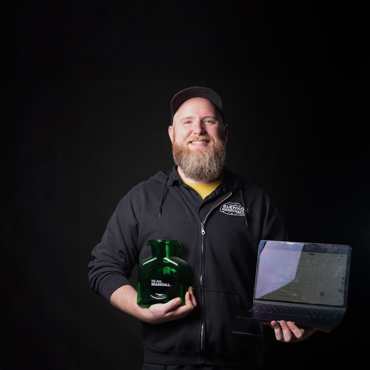 Man holding a green bottle and a laptop against a black background