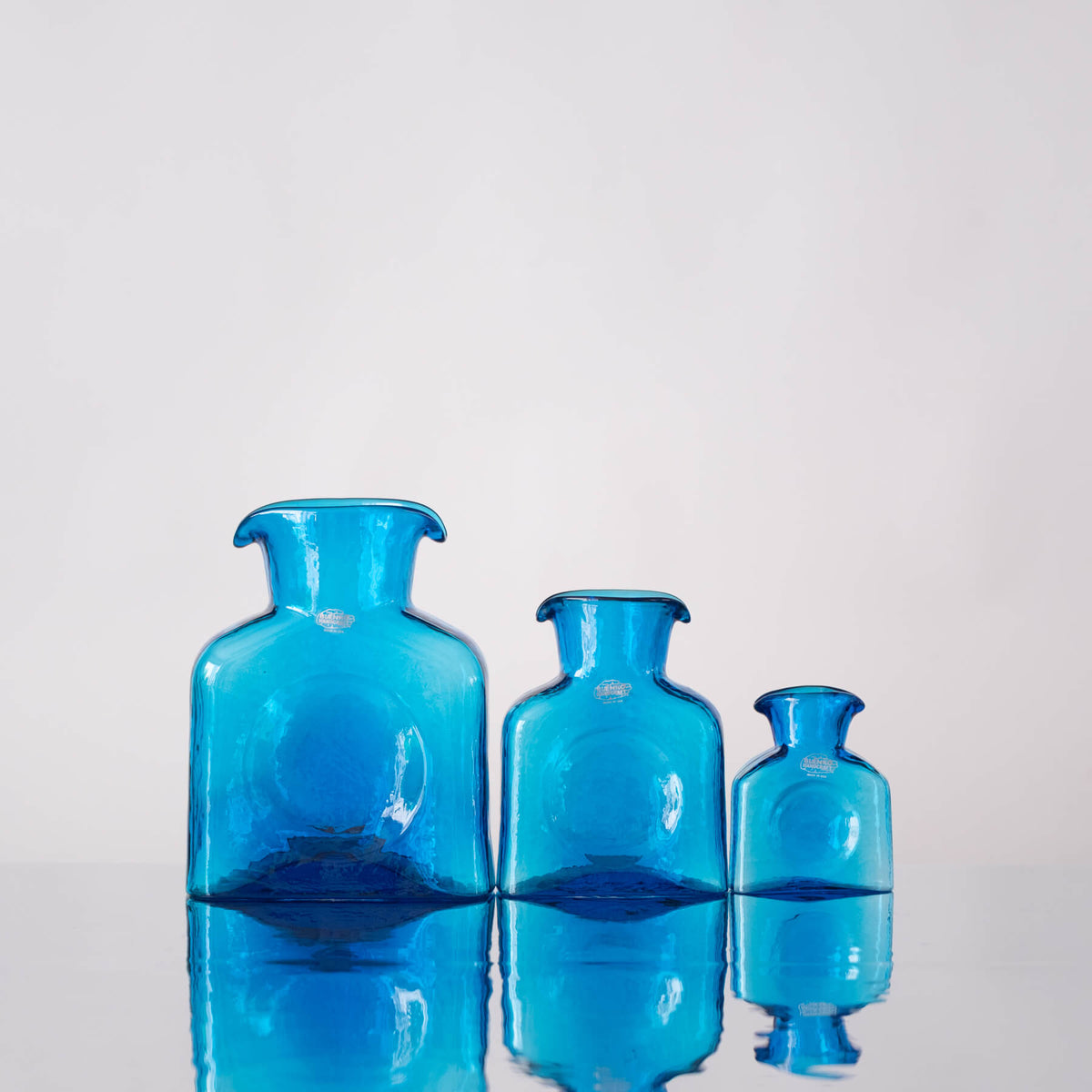 Three blue glass vases of different sizes on a reflective surface with a light gray background