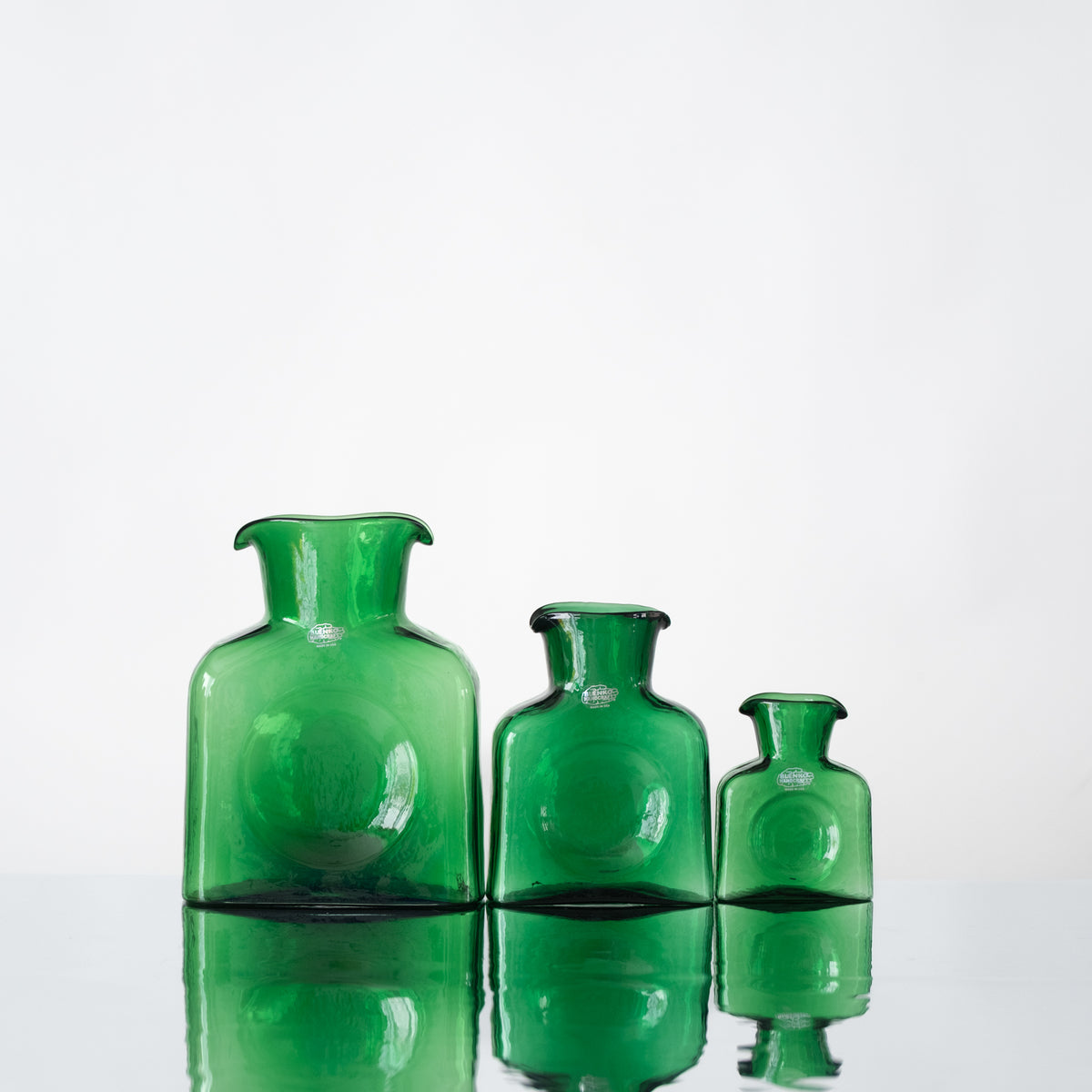 Three green glass bottles of varying sizes on a white background