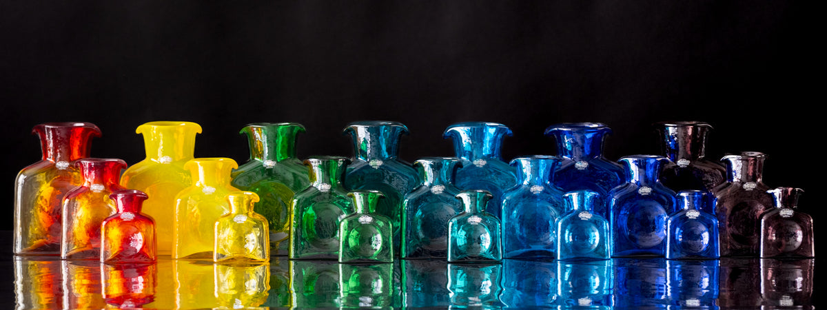 Colorful glass bottles arranged in a row on a reflective surface with a black background