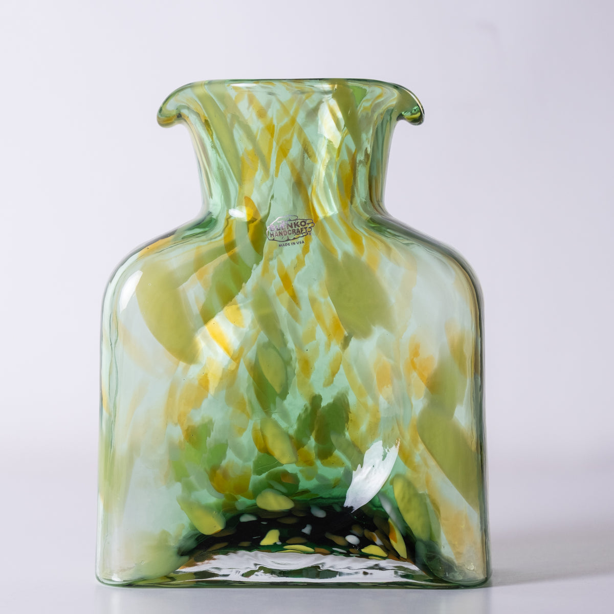 A hand-blown glass vase with a rounded body, flared neck, and small side tabs, featuring a marbled pattern of green, yellow, and white glass with a small 'Handmade in France' label near the neck.