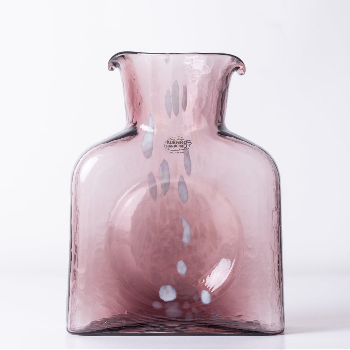 A translucent dusty pink glass vase with a flared rim and small vertical speckled details, photographed against a clean white background.