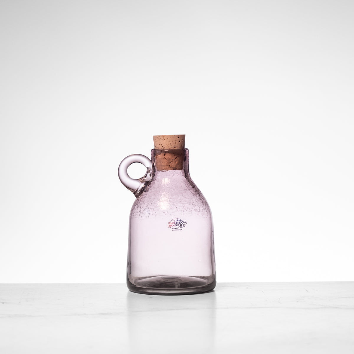 Purple glass carafe with a cork stopper on a white background