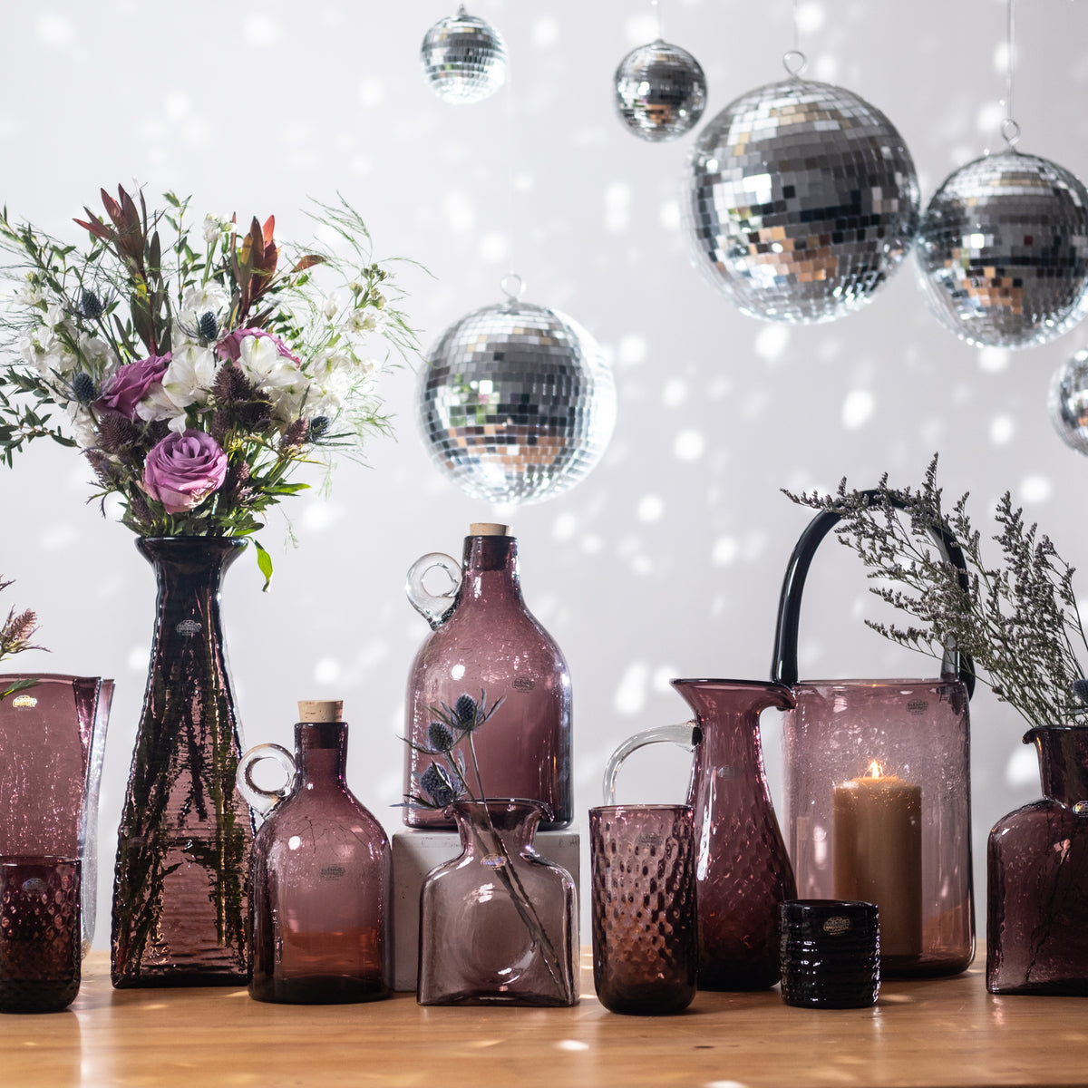 Decorative table setting with vases, bottles, and flowers against a disco ball and string light background.
