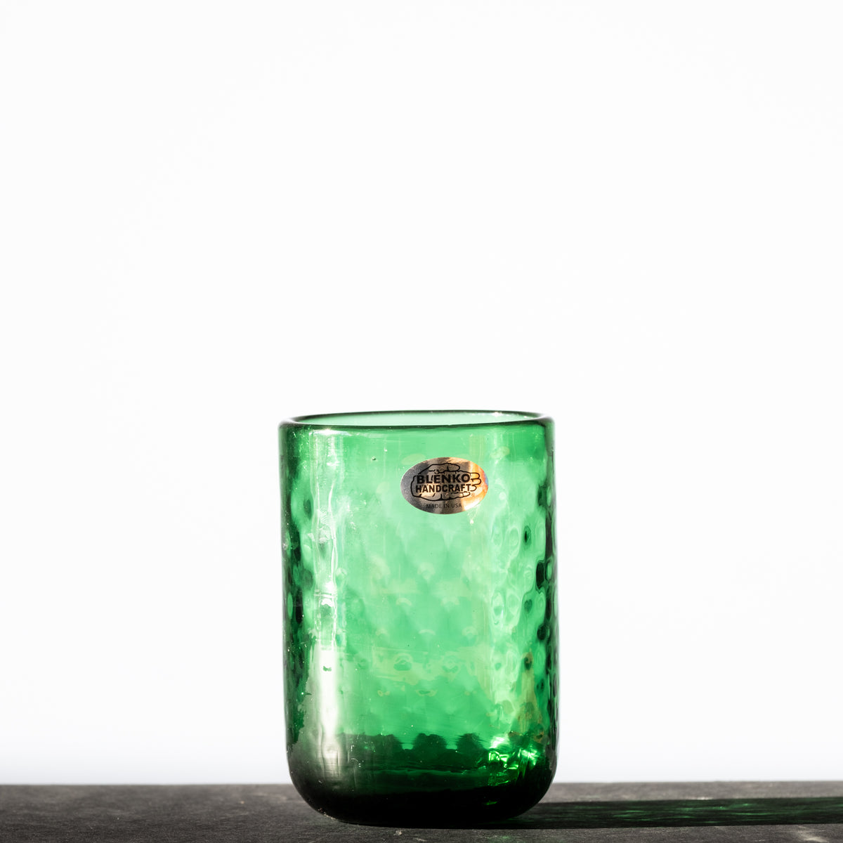 A green glass tumbler with a diamond optic pattern, displayed against a neutral background.