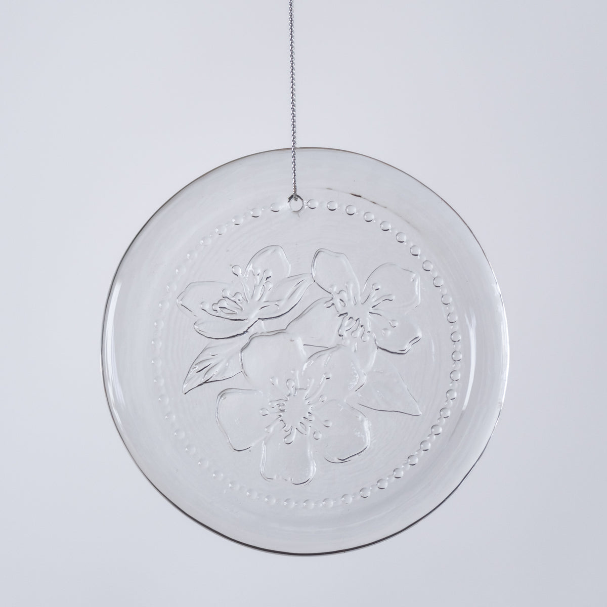 Clear circular decorative item with floral embossing on a light gray background