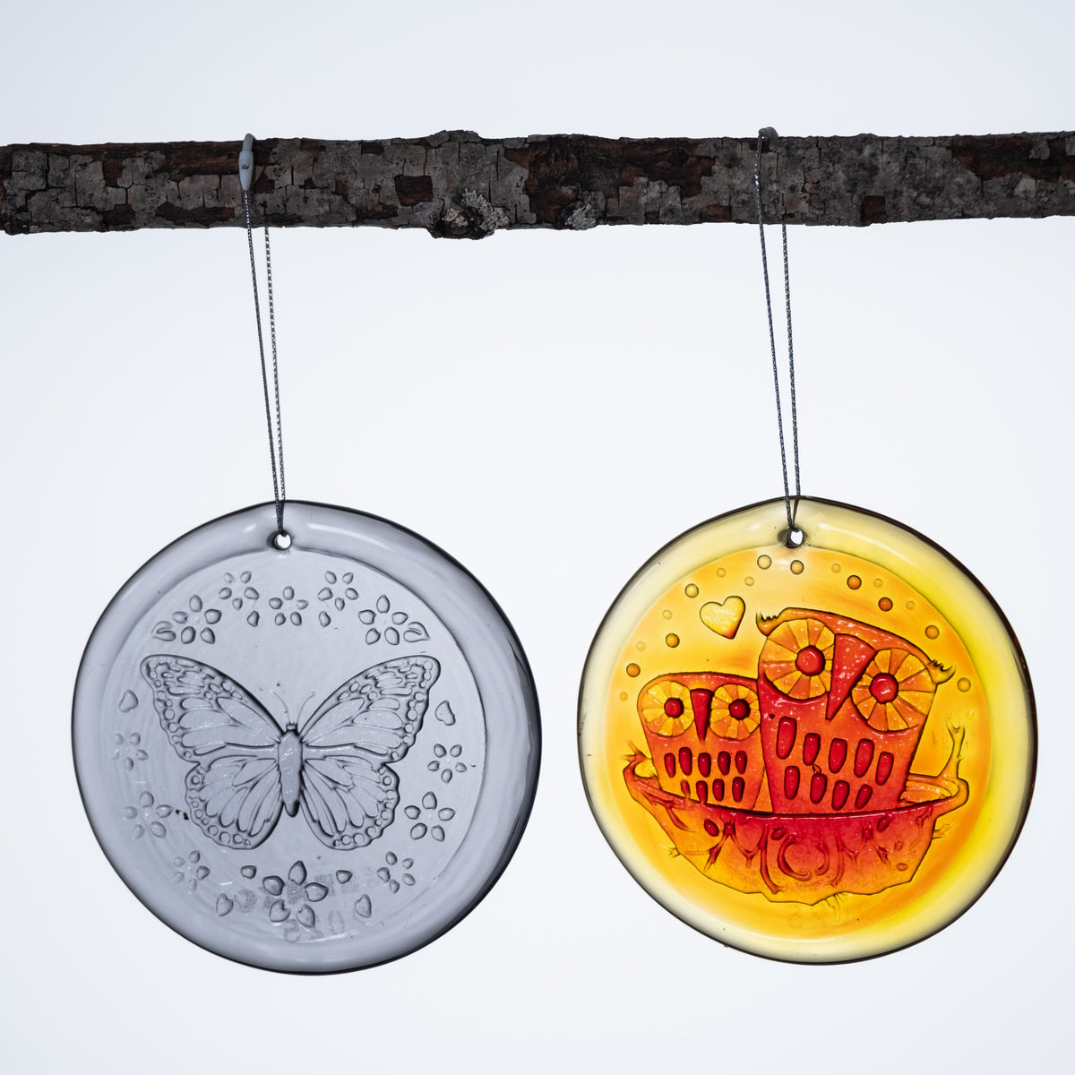 Purple butterfly nd orange owl suncatcher hanging from a branch on white background