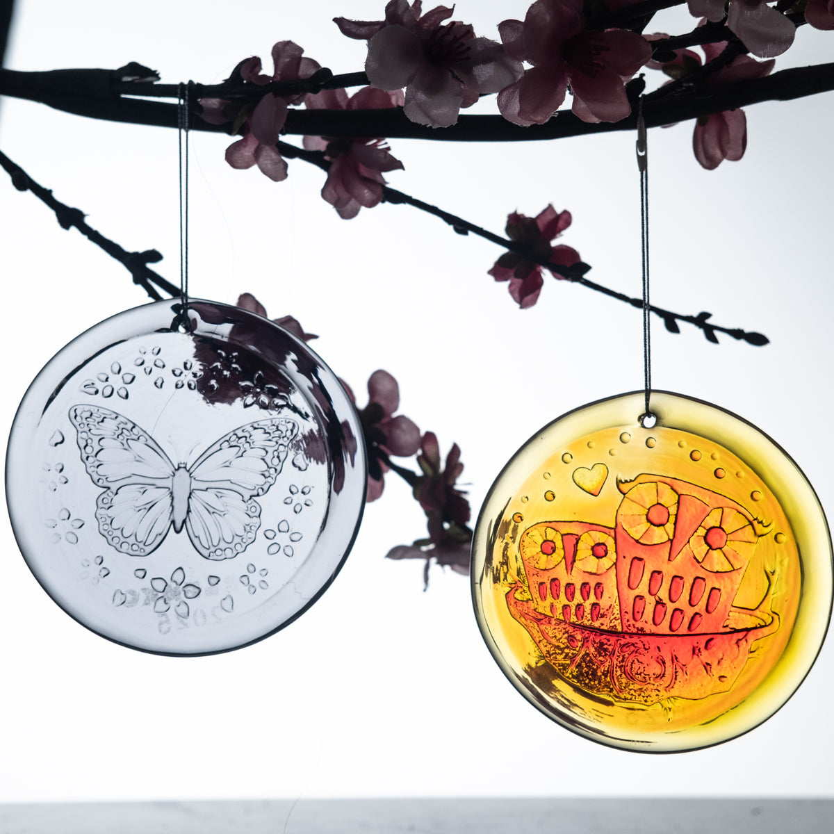 Purple butterfly nd orange owl suncatcher hanging from a branch on white background