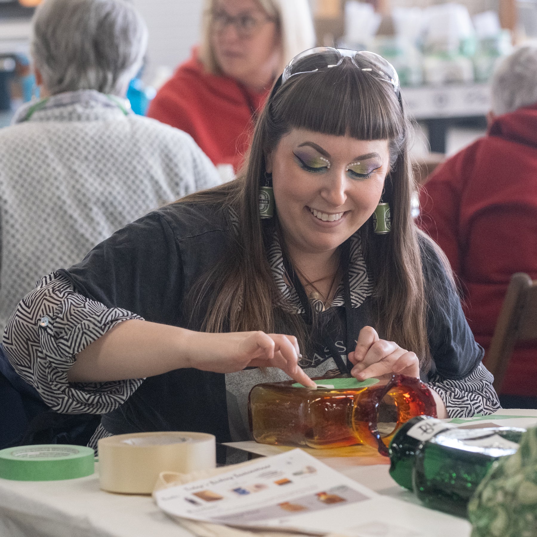 Woman at a table with craft materials, smiling and working on a project.